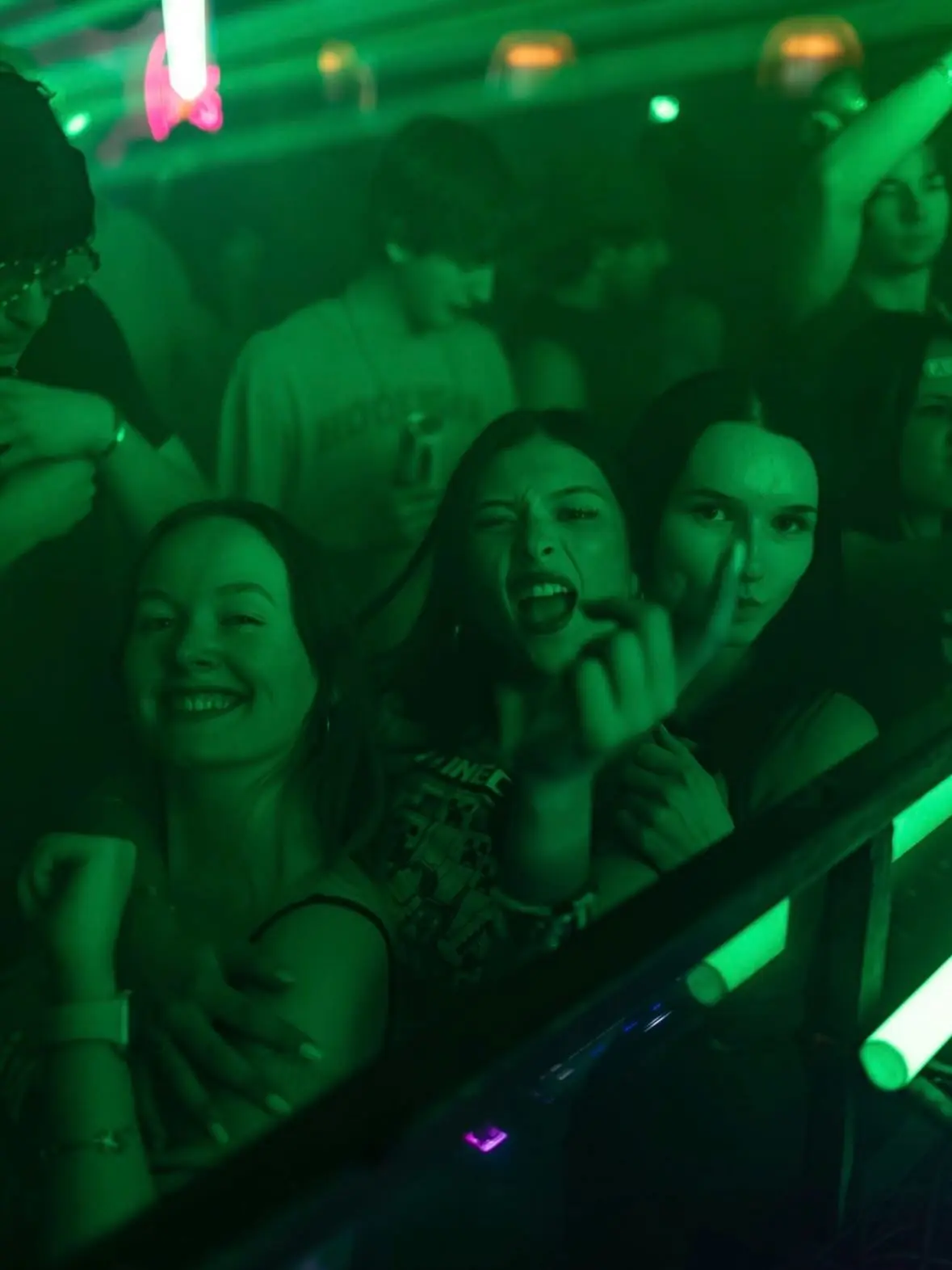 Three dancers leaning into the booth rail under saturated green light at City At Night.