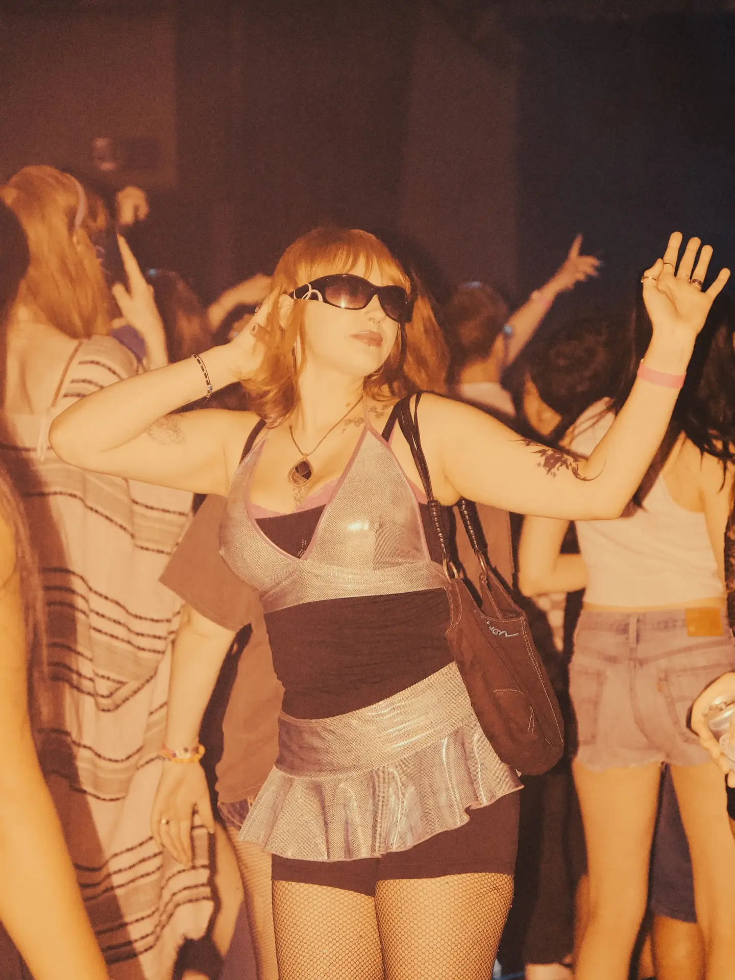 A dancer in silver sunglasses moving through the warm amber Frequency Fest crowd at Club SAW.