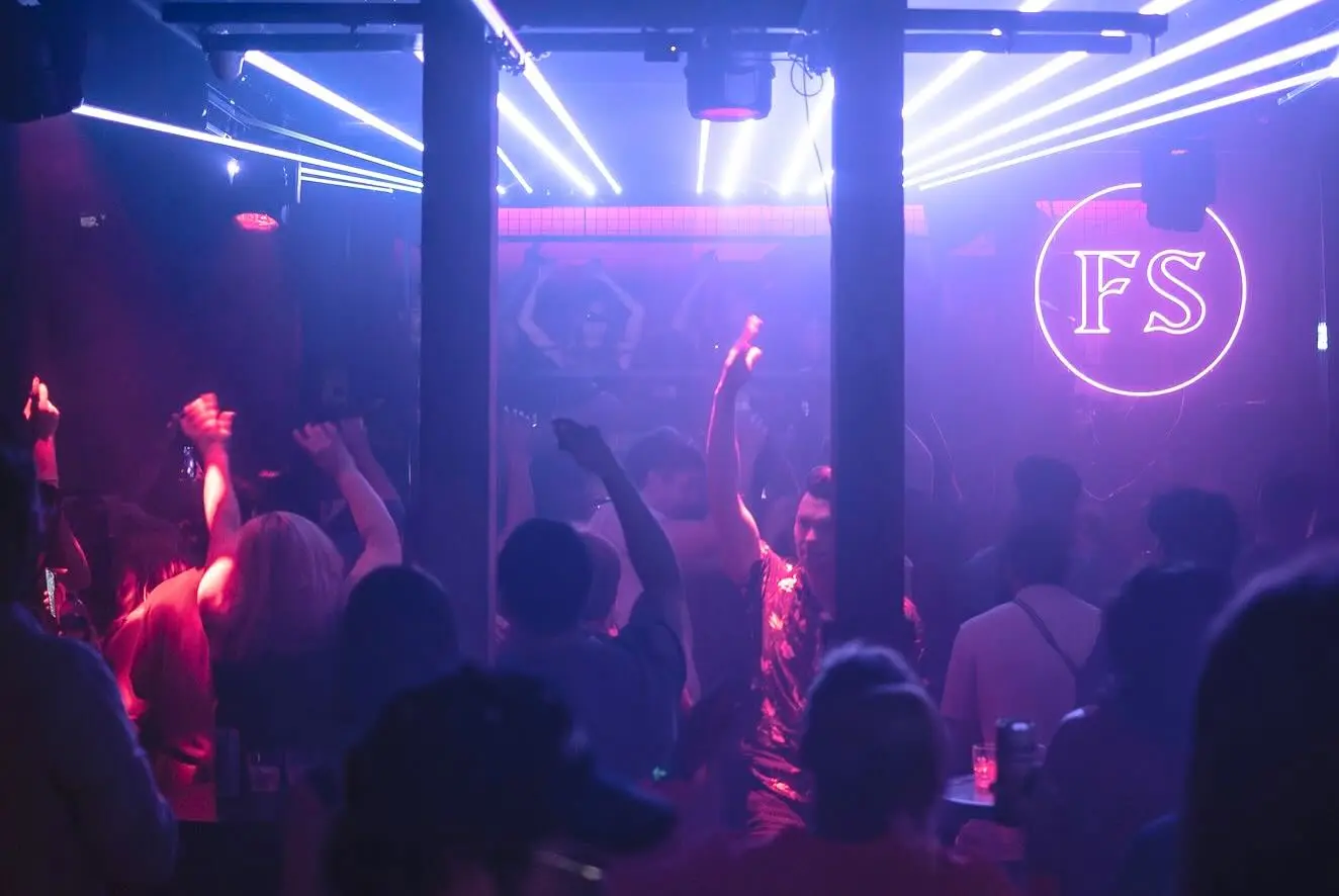Hands raised beneath blue and magenta beams with the Frequency Shift roundel glowing at GRIDWRKS.