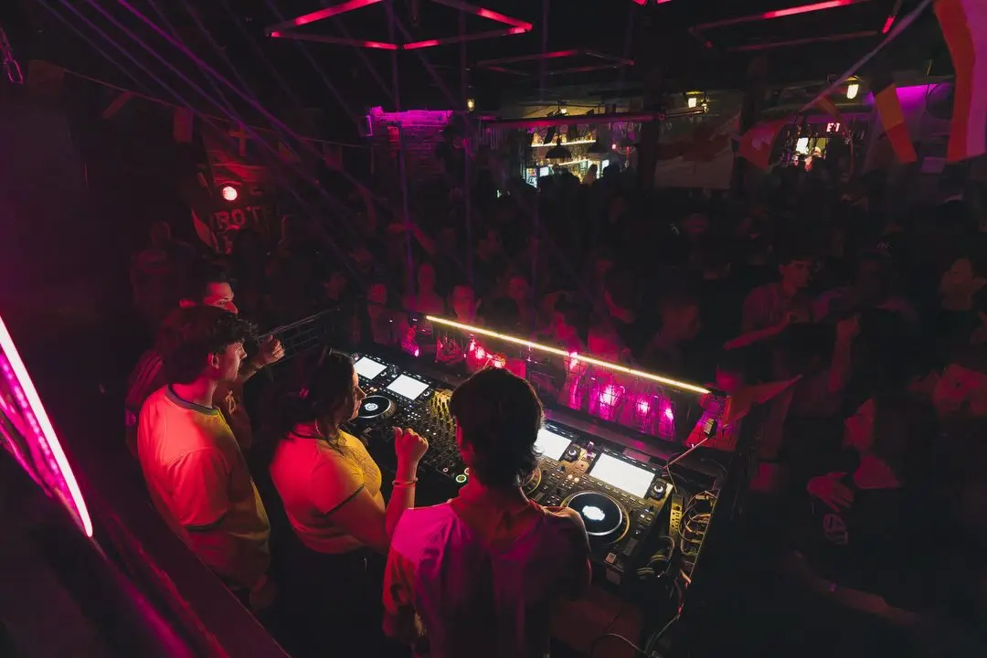 DJs framed by a packed GRIDWRKS dancefloor under deep red and pink lighting during the World Cup special.